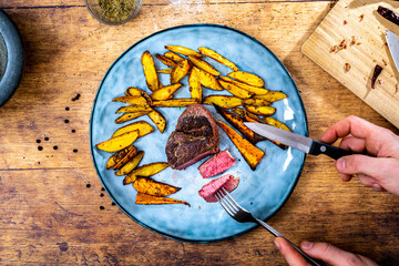 Man holding a homemade medium beef fillet steak piece with crisrpy golden brown potato wedges...