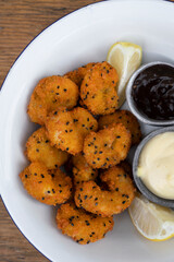 Seafood. Top view of a white bowl with fried panko shrimps with lemon, aioli and teriyaki dipping sauces, on the wooden table.