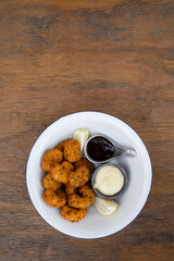 Seafood. Top view of a white bowl with fried panko shrimps with lemon, aioli and teriyaki dipping sauces, on the wooden table.