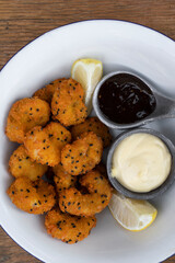 Seafood. Top view of a white bowl with fried panko shrimps with lemon, aioli and teriyaki dipping sauces, on the wooden table.
