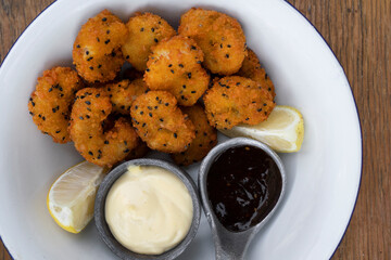 Seafood. Top view of a white bowl with fried panko shrimps with lemon, aioli and teriyaki dipping sauces, on the wooden table.