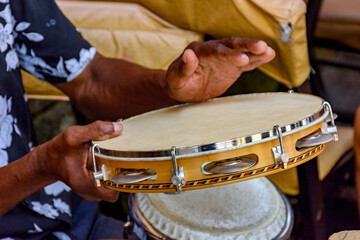 Hands and instrument of musician playing tambourine in the streets of Salvador in Bahia during a samba performance during carnival - obrazy, fototapety, plakaty