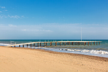 Fototapeta na wymiar Wooden sea pier in sun lights at the sandy beach
