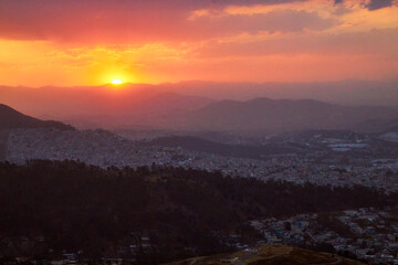 Obraz premium red sunset with city in the background, and mountains in foreground, sierra de guadalupe in state of mexico and mexico city