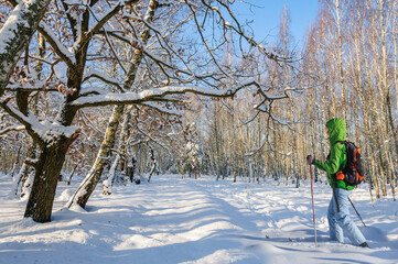 A girl in a green jacket rides on wooden skis in a snowy forest in Ukraine