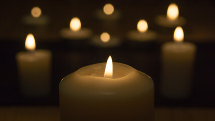One big candle in the foreground and blurred candle lights in the background in the dark