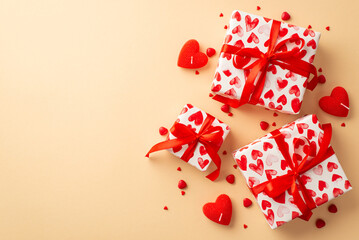 Valentine's Day concept. Top view photo of gift boxes in wrapping paper with heart pattern candles and sprinkles on isolated pastel beige background with copyspace