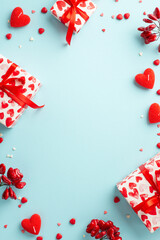 Saint Valentine's Day concept. Top view vertical photo of present boxes with ribbon bows heart shaped candles and sprinkles on isolated pastel blue background with copyspace in the middle