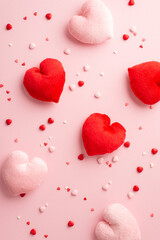 Valentine's Day concept. Top view vertical photo of heart shaped fluffy toys and sprinkles on isolated light pink background