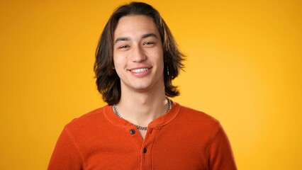 Portrait of smiling laughing, happy, handsome Hispanic gender fluid young man 20s wearing orange casual shirt isolated on yellow color background in studio. Sincere emotions lifestyle concept. - Powered by Adobe