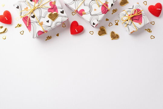 Valentine's Day concept. Top view photo of trendy present boxes heart shaped candles and golden confetti on isolated white background with blank space