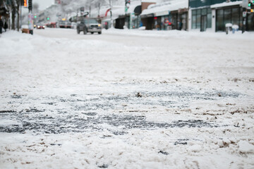 Snow covered city intersection, close up. Low angle view of main road not serviced or plowed with ice and slush. Stay at home and don't travel advice. East Vancouver, BC, Canada. Selective focus.