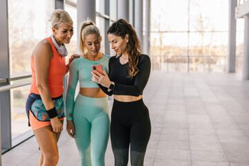 Three woman standing in the gym and look at the phone