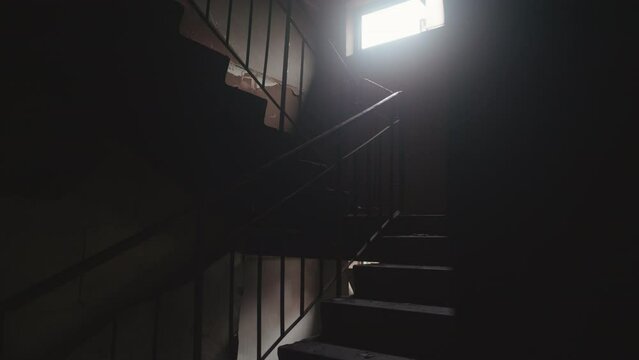 View from inside dark and ruined entrance stairs of residential building after being hit by russian missile. Damaged dark space. Sunlight outside the window. High quality 4k footage
