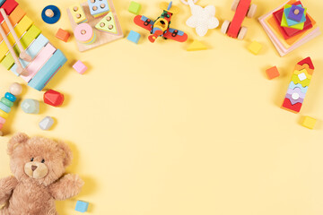 Fototapeta na wymiar Baby kids toys frame background. Teddy bear and wooden educational, sensory, sorting and stacking toys, colorful building blocks on yellow background. Montessori, susitainable toys. Top view, flat lay