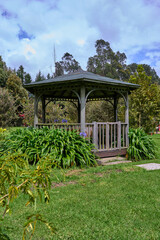 kiosk for picnic in the middle of the park. bushes surrounding the kiosk next to the grass. pergola with garden. green and open air area prepared for breakfast. 