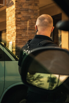 Vertical image of white male caucasian police officer standing outside cop vehicle as seen from within the trooper car. Officer looking away from camera.