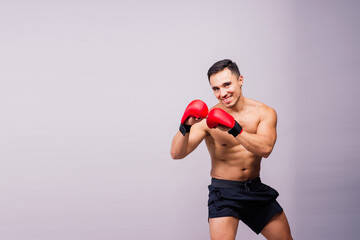 Muscular model sports young man in boxing gloves on grey background. Male flexing his muscles.