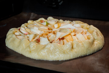 Uncooked galette, open pie with apples on tray in electric oven. French cuisine, homemade bakery, food, cooking and pastry concept