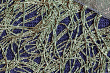 A green silk shawl with a fringe along the edge of the fabric against a dark blue woolen fabric....