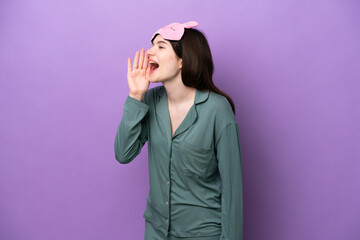 Young Russian woman in pajamas isolated on purple background shouting with mouth wide open to the...