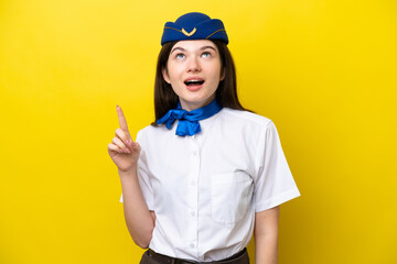 Airplane stewardess Russian woman isolated on yellow background pointing up and surprised