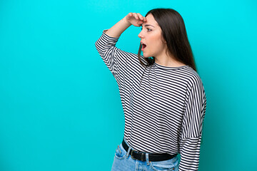Young caucasian woman isolated on blue background with surprise expression while looking side