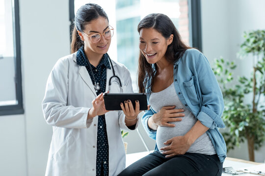 Female gynecologist doctor showing to pregnant woman ultrasound scan baby with digital tablet in medical consultation.