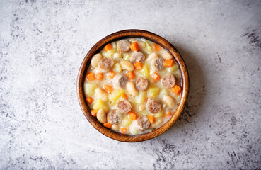 Potato carrot white bean soup with meat sausages in a bowl