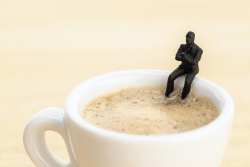 Businessman figurine sitting at a coffee cup. Coffee break concept
