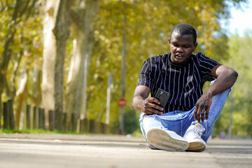 Naklejka na ściany i meble Portrait of a black young african male with a mobile in a park