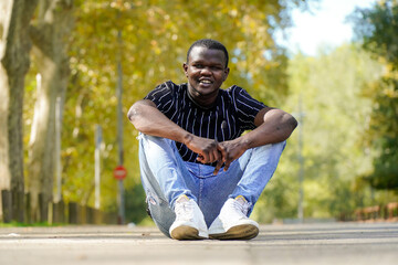 Obraz premium Portrait of a smiling black young african male siting and looking at camera in a park