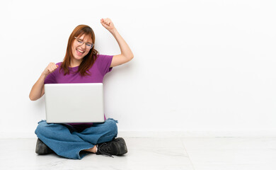 redhead girl with a laptop sitting on the floor celebrating a victory