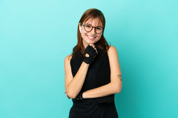 Redhead sport girl isolated on blue background with glasses and smiling