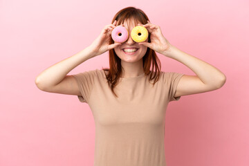 Redhead girl isolated on pink background holding donuts in eyes