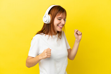 Redhead girl isolated on yellow background listening music and dancing