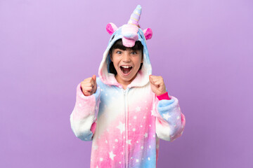 Little kid wearing a unicorn pajama isolated on purple background celebrating a victory in winner position