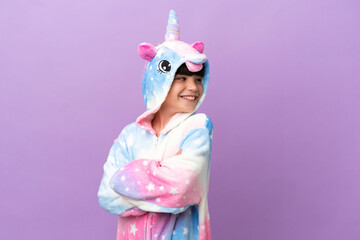 Little kid wearing a unicorn pajama isolated on purple background with arms crossed and happy