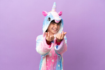 Little kid wearing a unicorn pajama isolated on purple background making money gesture