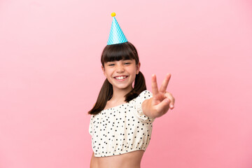 Little caucasian kid with birthday hat isolated on pink background smiling and showing victory sign