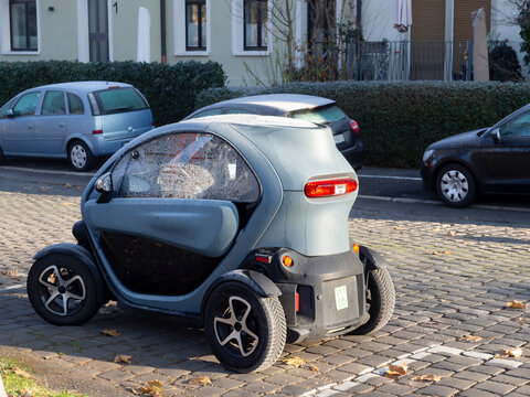 Coche peque&ntilde;o el&eacute;ctrico aparcado sobre calle de adoquines, recargable y sostenible con energ&iacute;a renovable, 2022 Alemania.