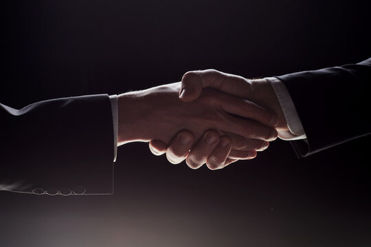 Photo Of Two Men In Suits Shaking Hands On A Black Background