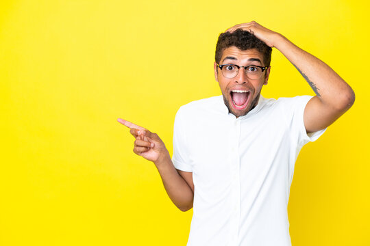 Young handsome Brazilian man isolated on yellow background surprised and pointing finger to the side