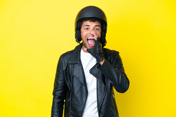 Young Brazilian man with a motorcycle helmet isolated on yellow background shouting with mouth wide...