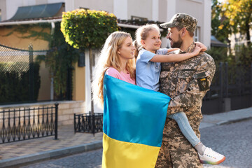 Soldier in military uniform reunited with his family and Ukrainian flag on city street, space for...
