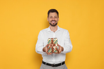 Happy man with gift box on yellow background