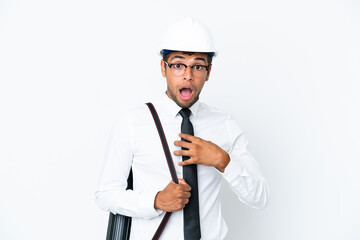 Architect brazilian man with helmet and holding blueprints surprised and shocked while looking right