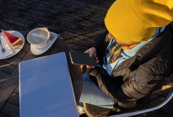 A girl sits in a street cafe with a mug of coffee, a dessert, a computer and a phone, Austria, Salzburg