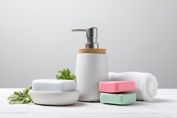 Fototapeta na wymiar Soap bars, bottle dispenser and towel on table against white background