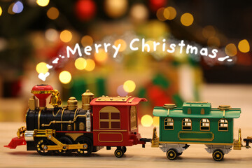 Greeting card with phrase Merry Christmas. Toy locomotive with rising steam in form of phrase Merry Christmas on wooden table against blurred lights
